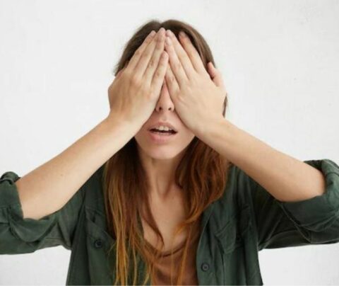 Mujer con camisa negra, tapandosé los ojos